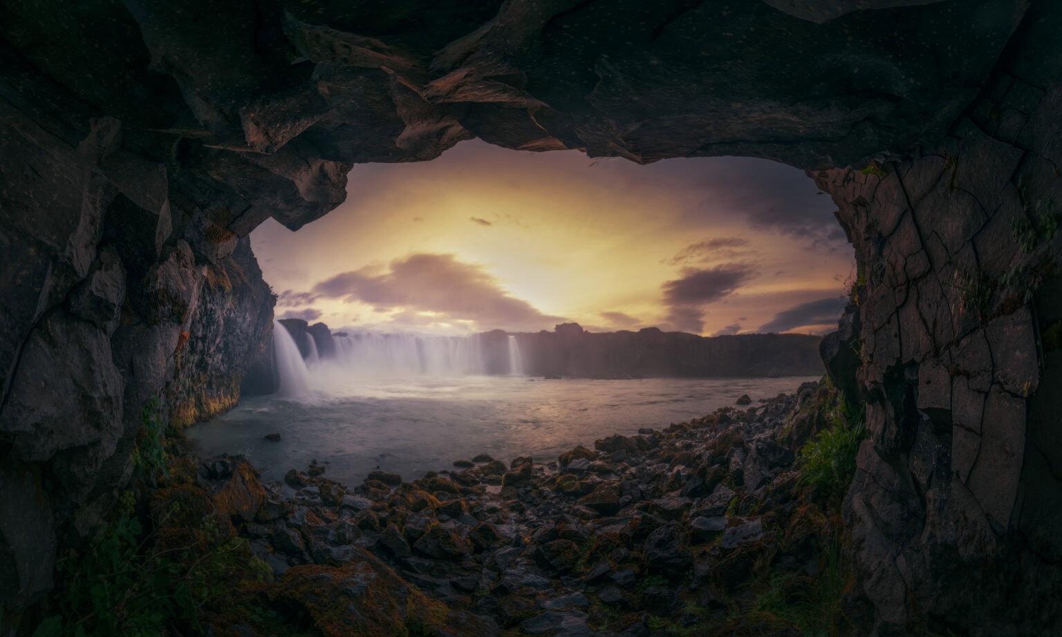 an image captured of water rolling off rocks during sunset, captured from within a cave.